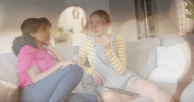 Kanepede konuşan iki farklı genç kızın üzerindeki ışık lekeleri. Arkadaşlık, gençlik, rahatlama ve yaşam tarzı, dijital olarak oluşturulmuş görüntü.