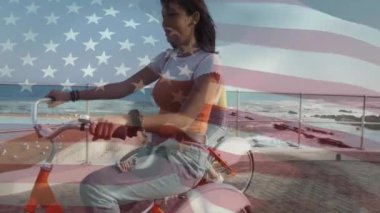 Gezinti güvertesinde bisiklete binen çift ırklı kadın üzerinde ABD bayrağı animasyonu. Vatanseverlik, yaşam tarzı ve dijital arayüz konsepti, dijital olarak oluşturulmuş video.