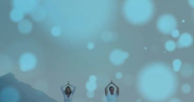 Kumsalda yoga yapan beyaz bir çiftin üzerinde hafif noktaların animasyonu. Spor, doğa ve dijital arayüz konsepti dijital olarak oluşturulmuş video.