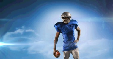 Heyecanlı Amerikan futbolcusunun bulutlu mavi gökyüzünde titreşimli ışıkla topu tutuşu. Fotokopi alanı olan profesyonel spor şablonu konsepti, dijital olarak oluşturulmuş resim.