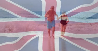 Union Jack sahilde yürüyen yaşlı bir çiftin bayrak animasyonu. Seyahat, tatil, vatanseverlik, milli gurur, turizm, deniz kenarı