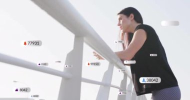 Korkuluklara yaslanmış, elinde şişeyle sosyal medya tebligatları taşıyan bir kadın var. Etkileyici, çevrimiçi, dijital, etkileşim, yaşam tarzı, teknoloji