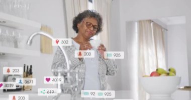 Akıllı telefon kullanan, mutfaktaki yaşlı kadın sosyal medya bildirimleriyle animasyon yapıyor. Teknoloji, yaşlılar, yaşam tarzı, iletişim, internet, uygulamalar