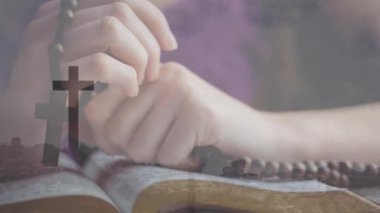 Dua eden eller, haç animasyonuyla İncil 'in üzerinde tespih taşır. İnanç, maneviyat, din, ibadet, dua, bağlılık.