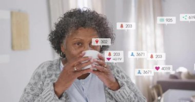 Kahve içen, sosyal medya bilgilendirmeleriyle çevrili yaşlı bir kadın. Rahatlama, teknoloji, dijital, yaşam tarzı, etkileşim, ekran