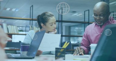 Kıdemli Afrikalı Amerikalı akıl hocası genç beyaz profesyonellerle belgeleri inceliyor. Her ikisi de ofis kalabalığının ortasında evrak işlerine odaklanıyor.