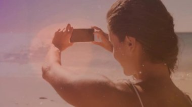 Sahilde parlak ışık animasyonuyla akıllı telefon kullanan bir kadın. Teknoloji, rahatlama, açık hava, tatil, yaz, deniz