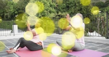 Paspaslar üzerinde yoga pratiği yapan, sarı ışık animasyonu yapan iki kadın. fitness, wellness, meditasyon, egzersiz, esneklik, rahatlama