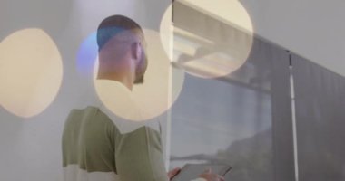 Tableti tutarken, arka planda bokeh ışıkları olan bir adam pencereden dışarı bakıyor. Teknoloji, tefekkür, kentsel, dijital, gece vakti, yenilik