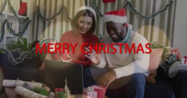Dizüstü bilgisayar kullanan şenlikli şapkalı çiftin mutlu noel mesajları animasyonu. Tatil, kutlama, teknoloji, kış