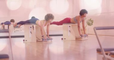 Pembe bokeh animasyon kaplamalı pilates aletleri üzerinde egzersiz yapan iki kadın. Spor, spor, egzersiz, sağlık, spor