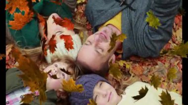 Sonbahar yaprakları, parkta yatan beyaz bir ailenin üzerinde. Aile ve doğa kavramı, dijital olarak üretilen video.