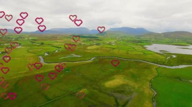 Arka planda dağlar olan yemyeşil bir arazide kalp animasyonu. Romantizm, doğa, aşk, manzara, açık hava, çevre