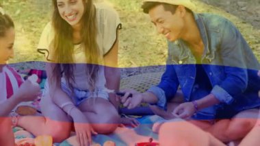 Piknik battaniyesinde oturan gülen arkadaşlar, açık havada renkli animasyonların tadını çıkarıyorlar. Kahkaha, birliktelik, keyif, eğlence, coşku, yaz