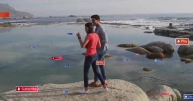 Deniz kenarında kayaların üzerinde duran, sosyal medya düğmeleri olan çift animasyon yapıyor. Sahil, açık hava, deniz manzarası, aşk, yaz