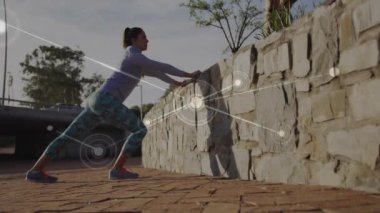 Taş duvara yaslanan, ağ bağlantılarıyla egzersiz yapan bir kadın. Fitness, egzersiz, teknoloji, sağlık, bağlantı, kablosuz