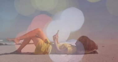 Kumsalda dinlenmek ve akıllı telefon kullanmak. Bokeh ışıkları animasyonu olan biri. Tatil, rahatlama, yalnızlık, dijital, yaz, tropik