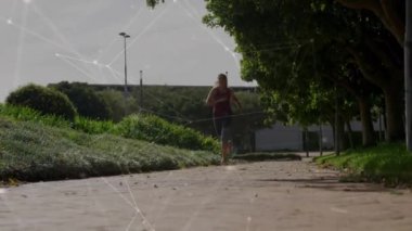 Park yolunda koşan, şebeke bağlantıları olan bir kadın yeşillik üzerine animasyon yapıyor. Fitness, egzersiz, teknoloji, dijital, bağlantı, doğa