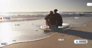 Sahilde oturan, sosyal medya bilgilendirmeleriyle çevrili bir çift. Tatil, rahatlama, teknoloji, internet, deniz kenarı, dijital