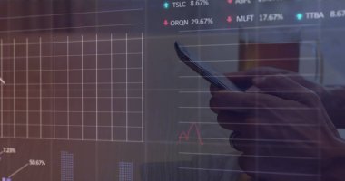 Akıllı telefon tutan, mali verileri inceleyen bir adam. Piyasa eğilimlerini gösteren grafikler ve yüzdeler, dikkatli analizleri yansıtıyor