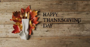 Çatal bıçak seti ve ahşap arka planda sonbahar yaprakları üzerindeki mutlu şükran günü metni. Şükran Günü, Amerikan geleneği ve dijital olarak üretilen imaj kutlaması.