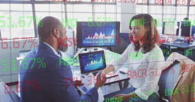 Çeşitli meslektaşlar ekranlardaki iş grafiklerini inceliyor. Kıdemli Afro-Amerikan erkek, kısa gri saçlı, takım elbiseli, uzun siyah saçlı genç bir Asyalı kadına tablet gösteriyor.