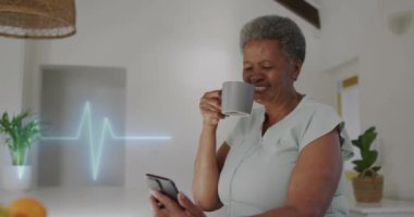 Evde akıllı telefon kullanan yaşlı, çift ırklı bir kadının kalp kardiyografisinin animasyonu. Tıp, emeklilik ve dijital arayüz konsepti dijital olarak oluşturulmuş video.