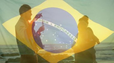 Plajda bebeği olan beyaz ebeveynler üzerine Brezilya bayrağı animajı. Yaşam tarzı, bayraklar ve vatanseverlik konsepti dijital olarak oluşturulmuş video.