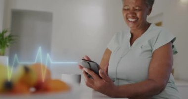 Akıllı telefon kullanan yaşlı melez kadının kalp şeklindeki kardiyografisinin animasyonu. Tıp, emeklilik ve dijital arayüz konsepti dijital olarak oluşturulmuş video.