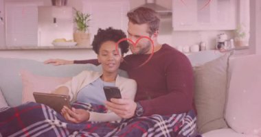 Kanepede akıllı telefon ve tablet kullanarak çeşitli çiftlerin üzerinde kalp ve ışık noktaları oluşturuluyor. Yaşam tarzı, ilişkiler ve ev hayatı konsepti dijital olarak oluşturulmuş video.
