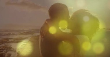 Deniz kenarında kucaklaşan melez çiftin üzerindeki ışık lekelerinin canlandırması. Yaşam tarzı, doğa ve dijital arayüz konsepti dijital olarak oluşturulmuş video.