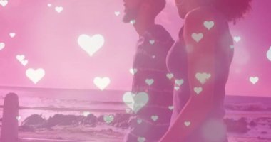 Deniz kenarında yürüyen melez bir çiftin üzerine düşen kalplerin animasyonu. Yaşam tarzı, doğa ve dijital arayüz konsepti dijital olarak oluşturulmuş video.