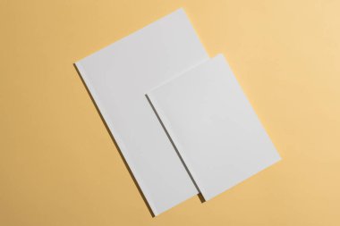 Blank white paper on a yellow background, with copy space. Ideal for graphic designers to showcase their work, the neutral setting emphasizes potential content. clipart