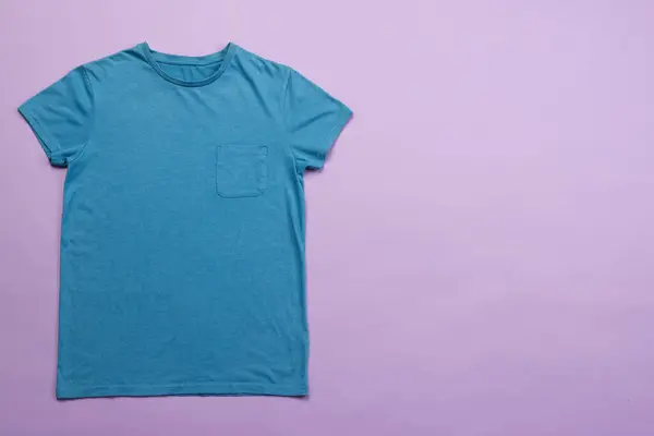 stock image A plain blue t-shirt is laid out on a purple background, with copy space. Its simple design makes it ideal for casual wear or for customization with prints or logos.