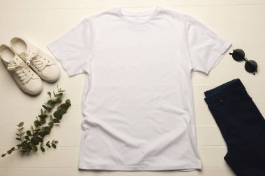 Sıradan beyaz spor ayakkabıların, koyu güneş gözlüklerinin ve lacivert pantolonların yanına düz beyaz bir tişört serilir, yeşil yapraklı bir dal doğaya dokunur, fotokopi alanı da vardır. Bu düzenleme bir cas için basit ve şık bir kıyafet seçimi önerir