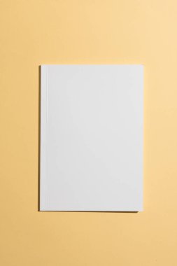 Sarı arkaplanlı boş beyaz bir kitap. Kopya alanı da var. Kapak resmi veya tasarımı için ideal olan kitap, yaratıcılık için temiz bir tuval sunuyor..
