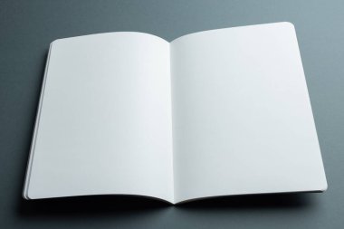 Açık boş bir defter, kopyalama alanı olan gri bir arkaplanda yatar. Temiz ve açık sayfalar nedeniyle tasarımcıların metin ve grafikleri taklit etmesi için ideal.