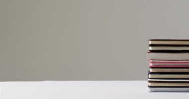 Çeşitli boyutlarda bir yığın kitap beyaz bir yüzeye oturur. Tarafsız arkaplan, ayarların eğitici ya da edebi temasını vurgular, yavaş çekim.