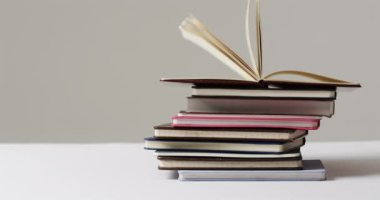 Bir yığın kitap düz bir arkaplanda, kopyalama alanı ile birlikte duruyor. Görüntü, eğitim, bilgi ve okuma sevgisini çağrıştırıyor..