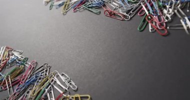 Renkli ataçlar koyu gri bir yüzeye, fotokopi alanı ile saçılmış. Düzenlemeleri ofis işleri, organizasyon ve malzeme temaları için uygun yaratıcı ve organize bir his sağlıyor..