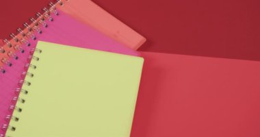 Kırmızı zemin üzerinde sarı bir defter barındıran canlı bir kompozisyon. Renkler ve kırtasiyeler, tasarım ve eğitim temaları için ideal yaratıcı veya akademik bir ortam önerir.