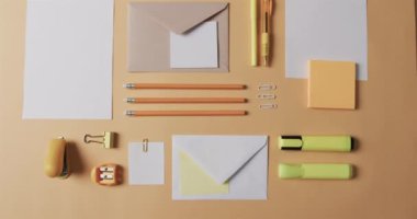 Çeşitli kırtasiye malzemeleri soluk turuncu bir yüzeye düzgün bir şekilde yerleştirilmiştir. Vurgulayıcılar, kalemler, zarflar ve ataçlar ofis işleri için bir düzen ve hazırlık hissi yaratır.