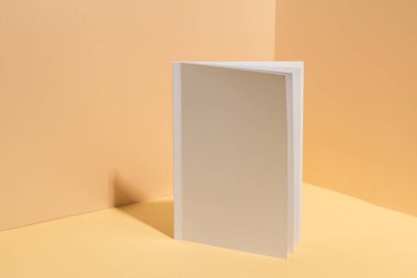 Boş beyaz bir kitap, fotokopi alanı olan bej bir arkaplan karşısında duruyor. Kapak tasarımlarını göstermek için idealdir, resim özelleştirme potansiyelini vurgular.