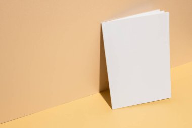Boş beyaz bir kitap, kopyalama alanı olan sarı bir yüzeyde dimdik duruyor. Kapak tasarımlarını sergilemek için idealdir. Kitabın basitliği yaratıcı özgürlüğe izin verir..