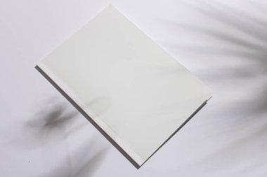Boş beyaz bir kitap, kopya alanı olan bir yüzeyde yatıyor. Kapak tasarımlarını sergilemek için ideal, sanatçılar ve tasarımcılar için temiz bir tuval..