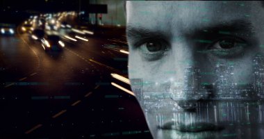 Dijital kodlu beyaz erkek yüzünü dikkatlice kapatıyor. Kısa koyu saçlı, açık tenli ve yeşil gözlü. Arka plan, gece hareket halindeki arabalardan gelen ışık çizgileriyle bulanık şehir manzarasını gösteriyor.