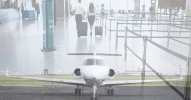 Composite image of plane at airport against businessman and businesswoman walking with trolley bags. Aviation business concept clipart