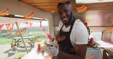 Image of hot dog icons over happy african american man preparing hot dog. Health, fitness and digital interface concept, digitally generated image. clipart