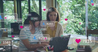 Asyalı öğretmen ve öğrenci, ikisi de bayan, dizüstü bilgisayara bakıyorlar. Öğretmen kahverengi saçlı, öğrenci gözlük takıyor, ikisi de ekrana odaklanmış.