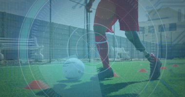 Futbol topu ve koni ile çift ırklı atlet eğitimi. Kırmızı şort, beyaz çorap ve krampon giyip, top kontrolüne odaklanmış.